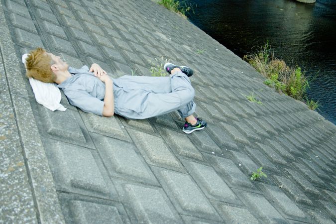 Man in blue boiler suit laying on concrete ground