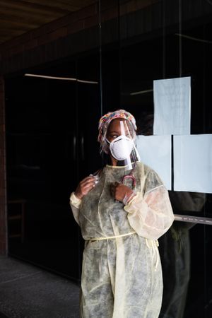 Three quarter shot of woman nurse wearing PPE standing in front of office door