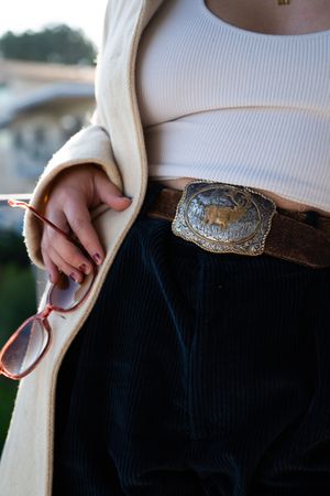 Cropped close up of woman holding sunglasses wearing vintage belt buckle