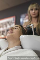 Female with head back in sink at hairdressers having her hair washed, vertical 5o8v14