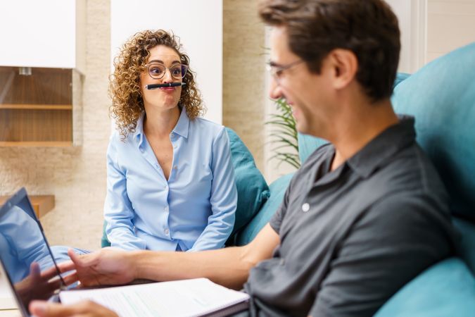 Cheerful woman playing with pen over mouth while sitting with man in living room