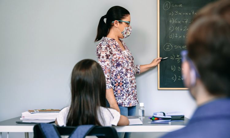 Teacher with mask explaining exercises in math class