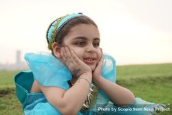 Girl in blue princess dress smiling and sitting on green field bYrqY0