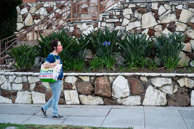 Side view of man walking down sidewalk carrying grocery bag