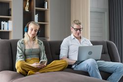 Young woman sitting on sofa with father using laptop