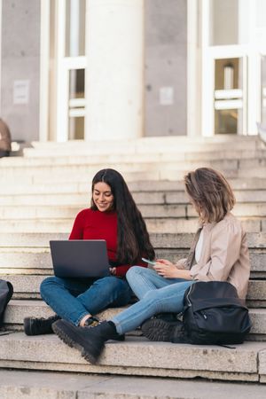 Two students sitting on the stairs of the college with a laptop and mobile.