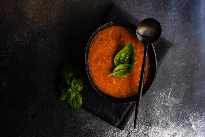 Dark bowl of gazpacho soup with basil leaves
