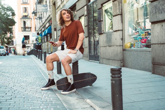 Amused man with longboard talking on phone while resting on street