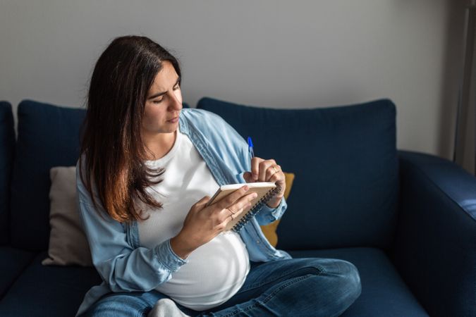 Pregnant woman taking notes in notebook at home
