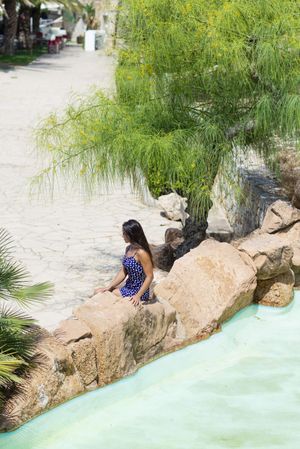 Above view of a pretty hispanic woman sitting on rock next to a pond