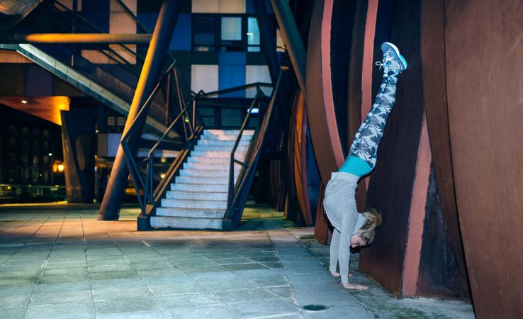 Woman doing handstand exercise against of sheet metal wall in the city at night