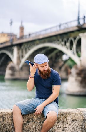 Bearded young man in casual wear using smartphone while walking on quay