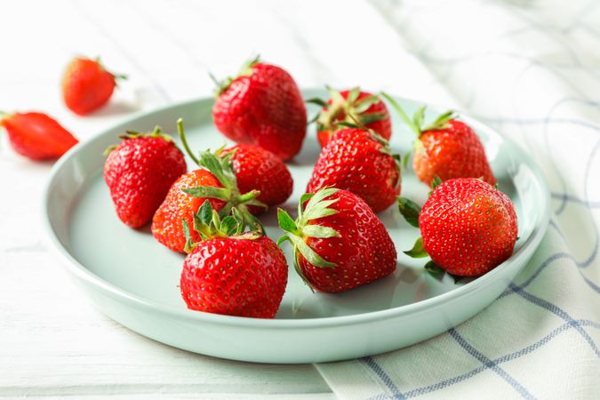 Plate with fresh strawberries and kitchen towel on bright wooden background, closeup and space for text