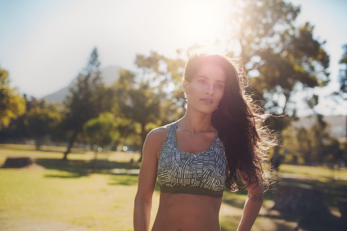 Attractive young woman in sportswear standing outdoors in a park on a bright sunny day