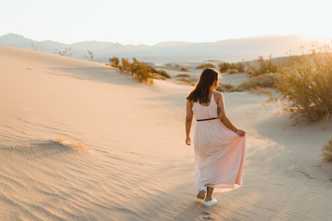 Back view of young woman walking in desert leaving footprints in dry sandy dunes in Death Valley