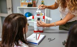 Teacher in a robotics class explaining how connect solar panel on recycled toy robot