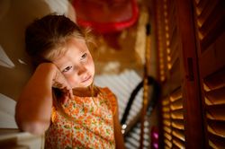 Bored girl leaning on hand against shutters in sunbeams
