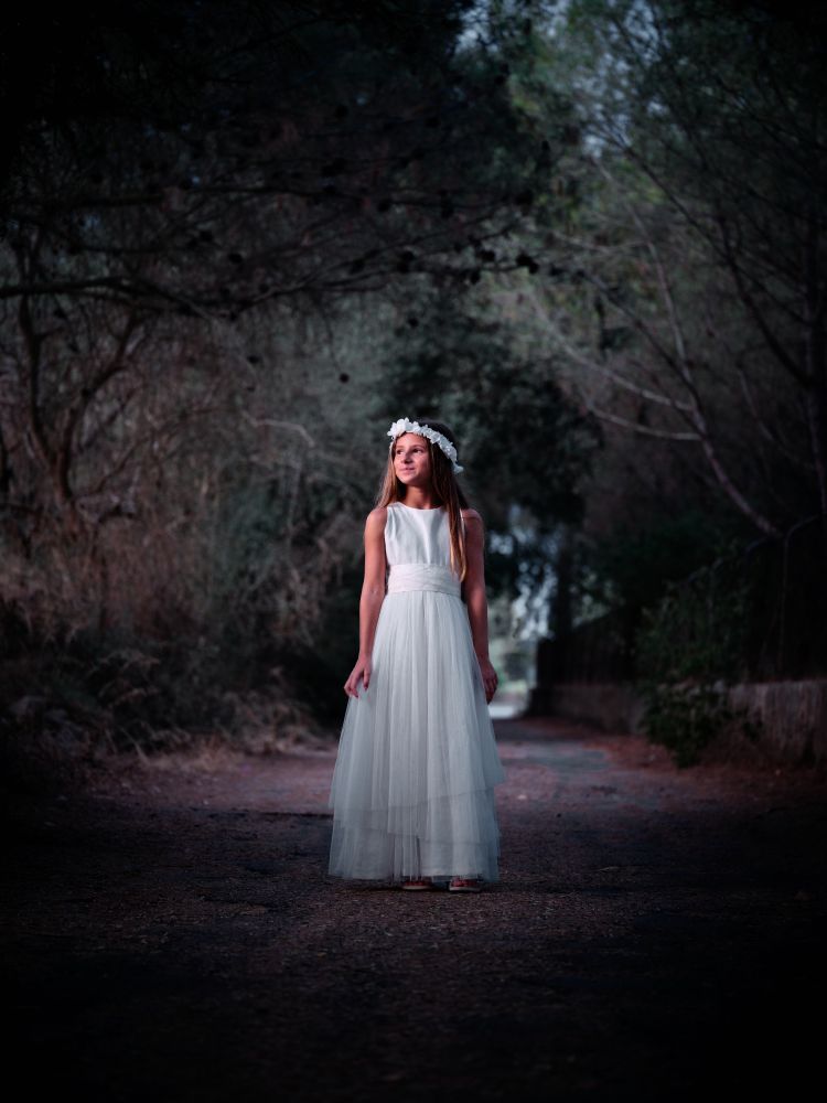 Elegant girl in white dress standing on dark path with closed gr