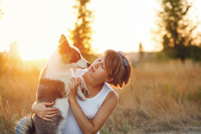 Whimsical woman holding her husky dog in field at dusk with space for text
