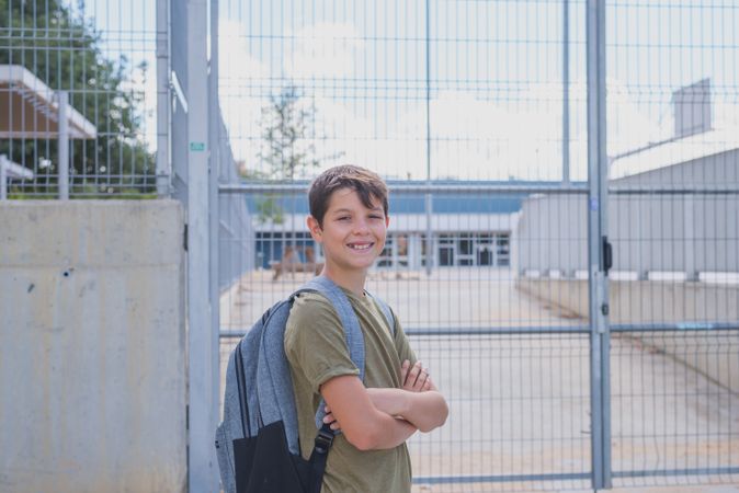 Happy teenager in backpack smiling outside school gate