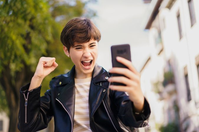 Excited and spirited youth joyfully celebrating while using their smartphone in an urban setting