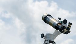 Brass telescope against cloudy sky background.