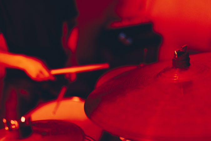 Anonymous man with drumsticks playing on drums in redness
