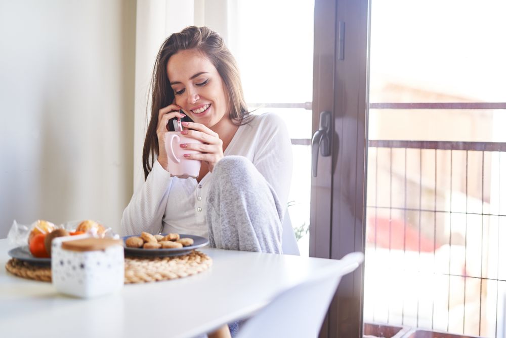 Smiling woman with smartphone eating at table at home