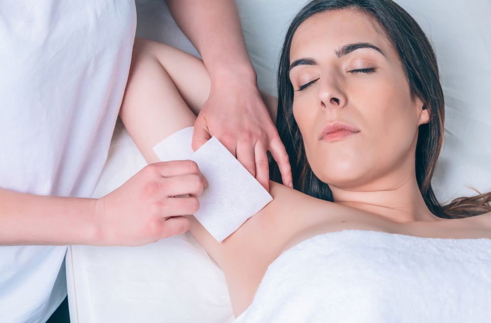 Aesthetician's hands waxing woman's underarm in a beauty salon