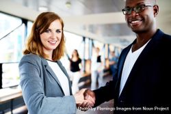 Black male and white female business associates shaking hands in hallway 0L2wD4