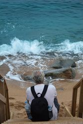 Back view of middle aged man in light shirt sitting on wooden steps by the sea bDJyp5