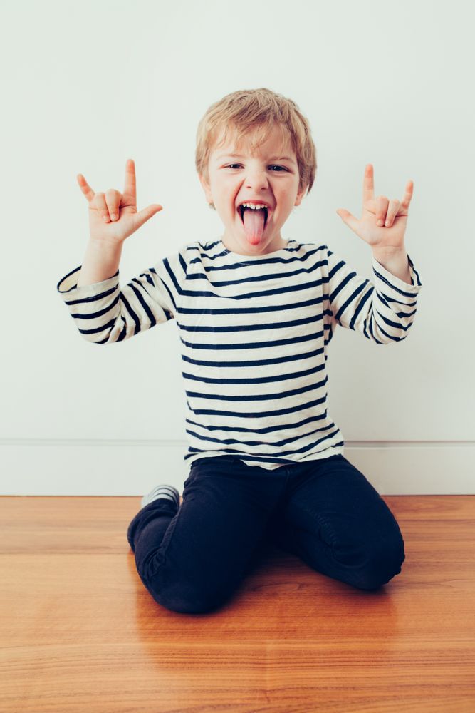 Boy showing tongue and rock gesture on floor