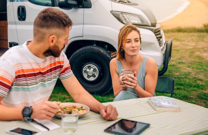Man and woman sitting on outdoor table by parked motorhome