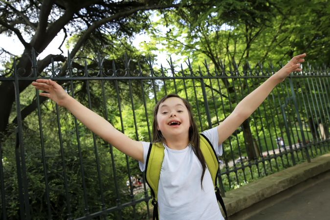Young child raising her arms up outdoors near a park