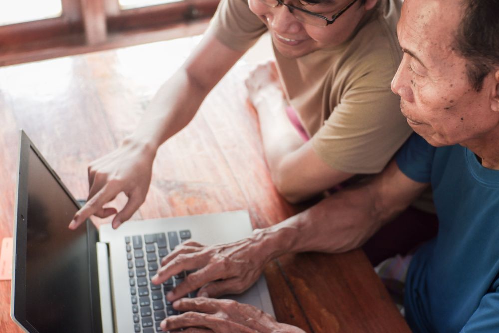 Happy adult son teaching older father using laptop
