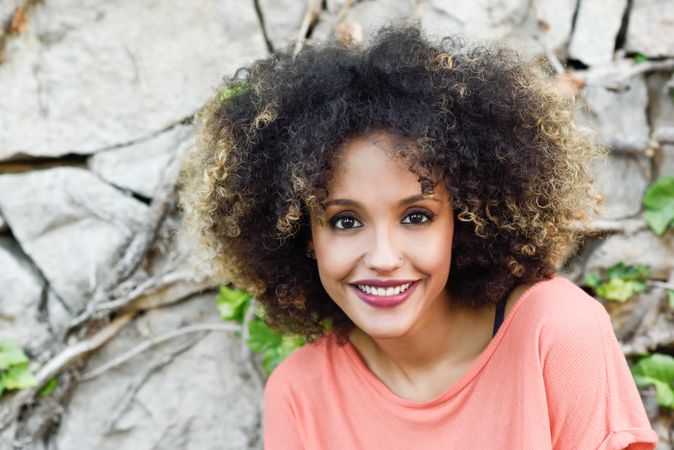 Portrait of smiling Black woman with afro hairstyle in front of stone wall