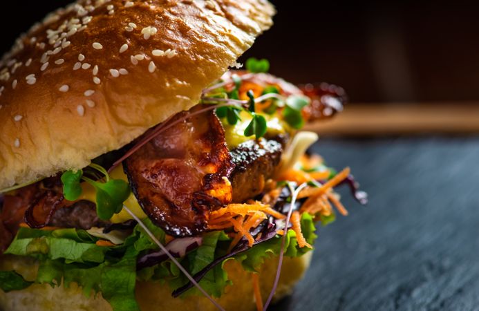 American hamburger with meat, cheese and different vegetables on dark rustic background with copy space