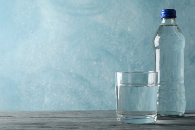 Glass of water with bottle in blue room, copy space