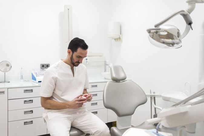 Bearded dentist man holding a jaw model while waiting for patient