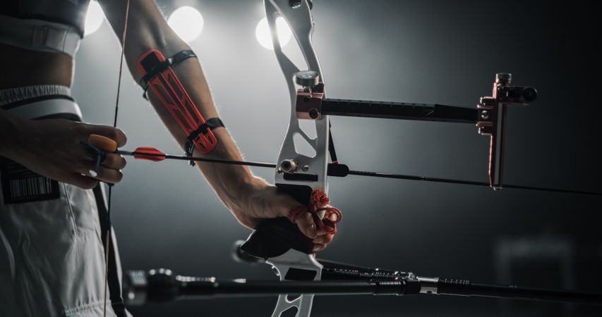 Low Angle Shot Of an Anonymous Female Archer Holding a Modern Compound Bow, Aiming at a Target. Young Athlete Drawing the Arrow in a Stadium Competition or a Dark Studio for Advertising