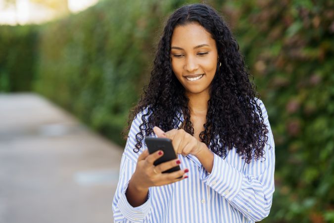 A young woman happily engages with her smartphone in the outdoors, surrounded by nature