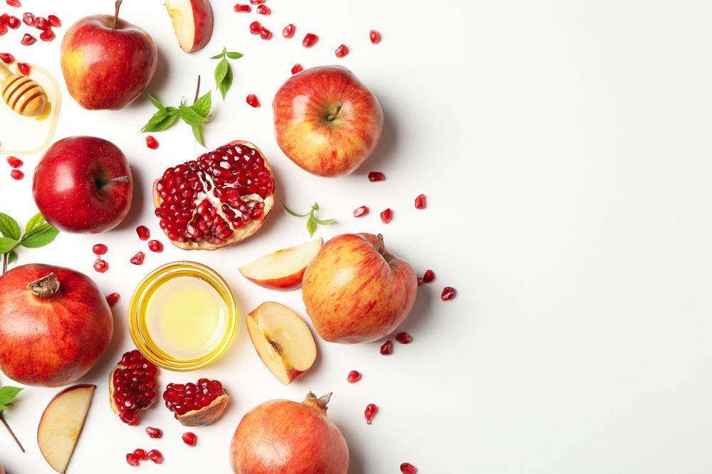 Scattered apples, pomegranates, and honey pot with copy space