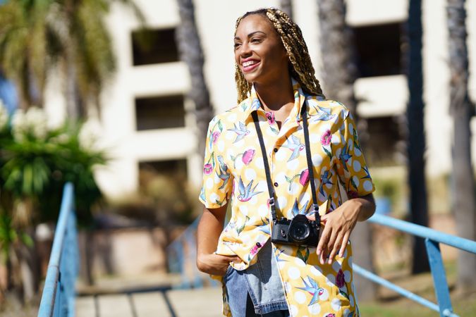 Female photographer in yellow printed pattern on pedestrian bridge by palm trees
