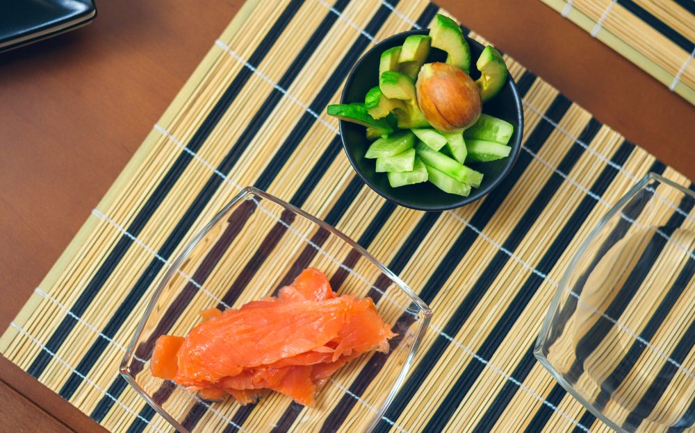 Top view of bowls with avocado, cucumber and salmon cut ready to prepare sushi