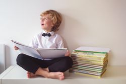 Happy schoolboy reading book in room