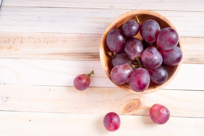 A bowl of red grapes sits on a wooden table