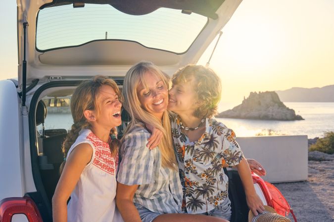 Happy mother and children sitting together on car trunk