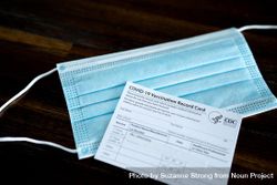 Medical mask and vaccination card laying on table bYWlX5