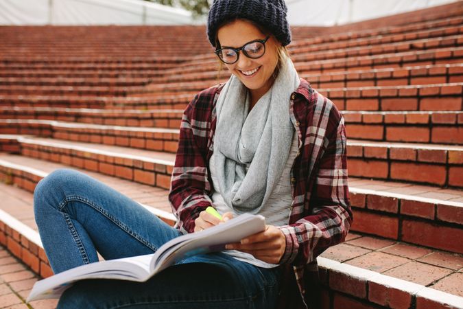Female college student sitting on campus with pen and book