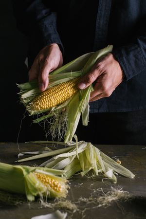 Crop person peeling corn over table